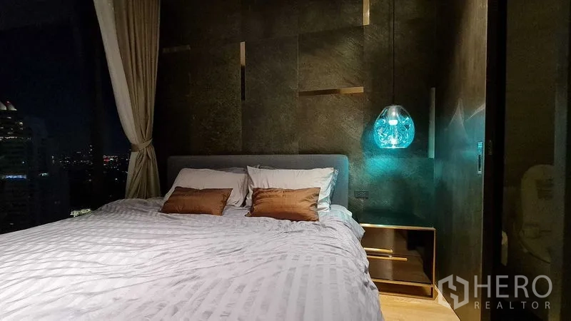 Condominium for rent in Watthana, Bangkok - Cozy bedroom at night with a pendant light and dark feature wall.