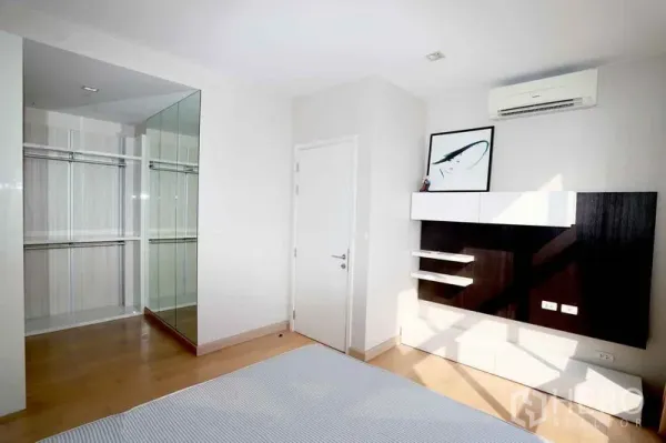 Condominium for rent in Khlong San, Bangkok - Bright bedroom with built-in TV wall, air conditioning, and a mirrored walk-in closet in a Bangkok condo.