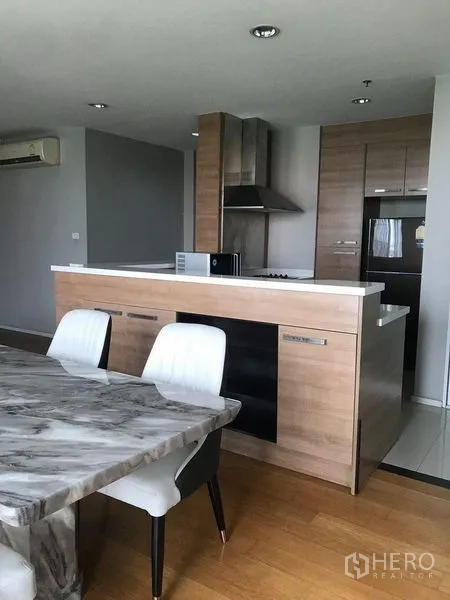 公寓 出租在Watthana, Bangkok - 开放式客餐厅内的厨房岛台与木质橱柜，旁为大理石餐桌。