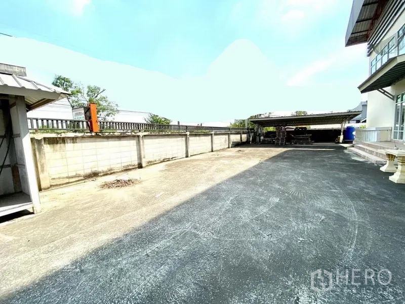 Warehouse for rent in Lam Luk Ka, Pathum Thani - Paved yard beside the warehouse with boundary wall and covered work area.