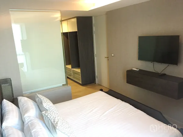 Condominium for rent in Watthana, Bangkok - Cozy bedroom with wall-mounted TV, frosted glass partition to the bathroom, and built-in wardrobe.