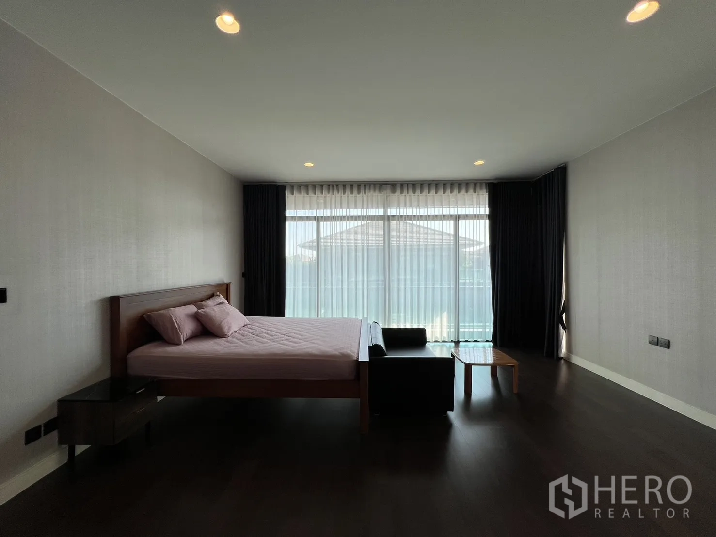 Detached House for rent or sale in Bang Kapi, Bangkok - Large master bedroom with dark wood floors and access to a balcony.