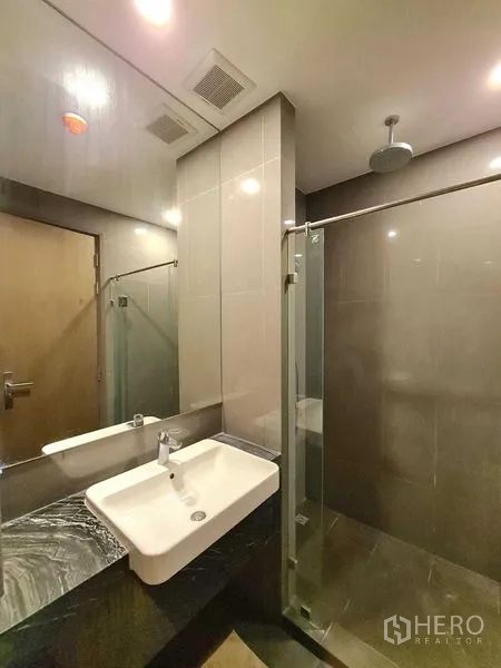 Condominium for rent in Bang Rak, Bangkok - Contemporary bathroom with glass shower enclosure, rain shower and vanity.