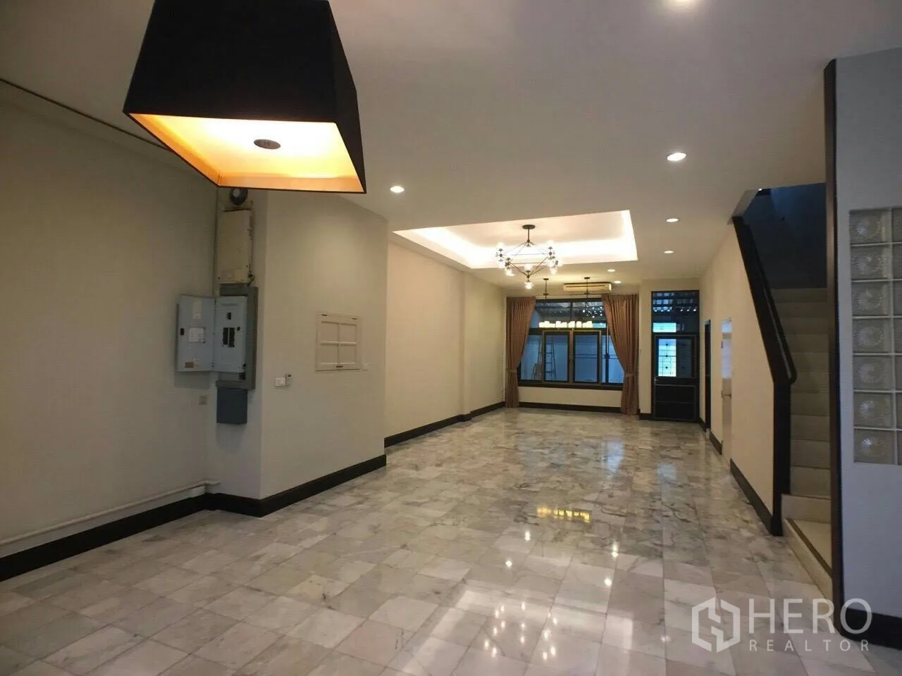 Townhouse for rent in Khlong Toei, Bangkok - Open-plan living area with marble floors, recessed lighting, staircase, and multiple chandeliers.