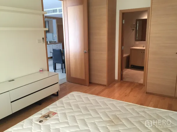 Condominium for rent in Sathon, Bangkok - Bedroom view toward the ensuite bathroom and open dining/kitchen area with wooden doors and flooring.