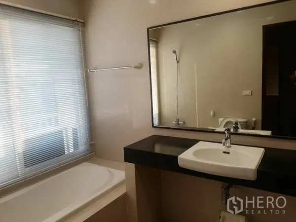 Condominium for rent in Watthana, Bangkok - Modern bathroom with bathtub, large mirror, countertop basin and window blinds.