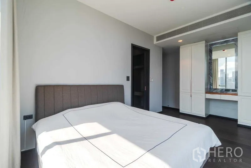 Condominium for rent or sale - Sunlit bedroom with upholstered bed facing dressing area with wardrobes and vanity.
