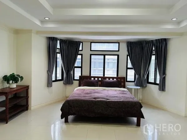 Home Office for rent in Watthana, Bangkok - Spacious bedroom with bay windows, gray curtains, and a wooden bed on glossy tile floors.