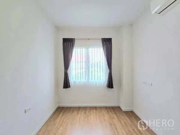 Detached House for rent in Samut Prakan - Bright empty room with wood-look flooring, curtained window and wall-mounted AC.