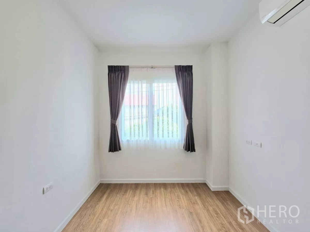 Detached House for rent in Samut Prakan - Bright empty room with wood-look flooring, curtained window and wall-mounted AC.