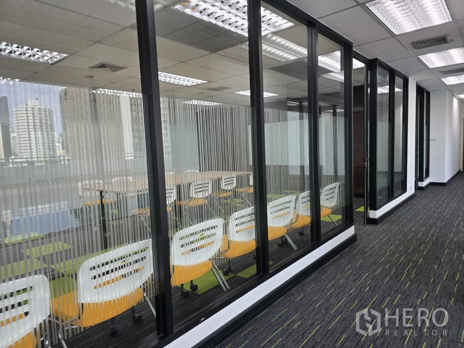 Office Space for rent in Watthana, Bangkok - Glass-partitioned room with a row of chairs and city reflections on the glass.
