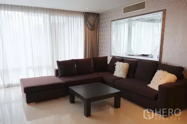 Condominium for rent in Watthana, Bangkok - Bright living room with L-shaped sofa, full-height curtains and a decorative framed mirror.