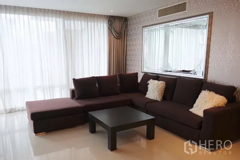 Condominium for rent in Watthana, Bangkok - Bright living room with L-shaped sofa, full-height curtains and a decorative framed mirror.