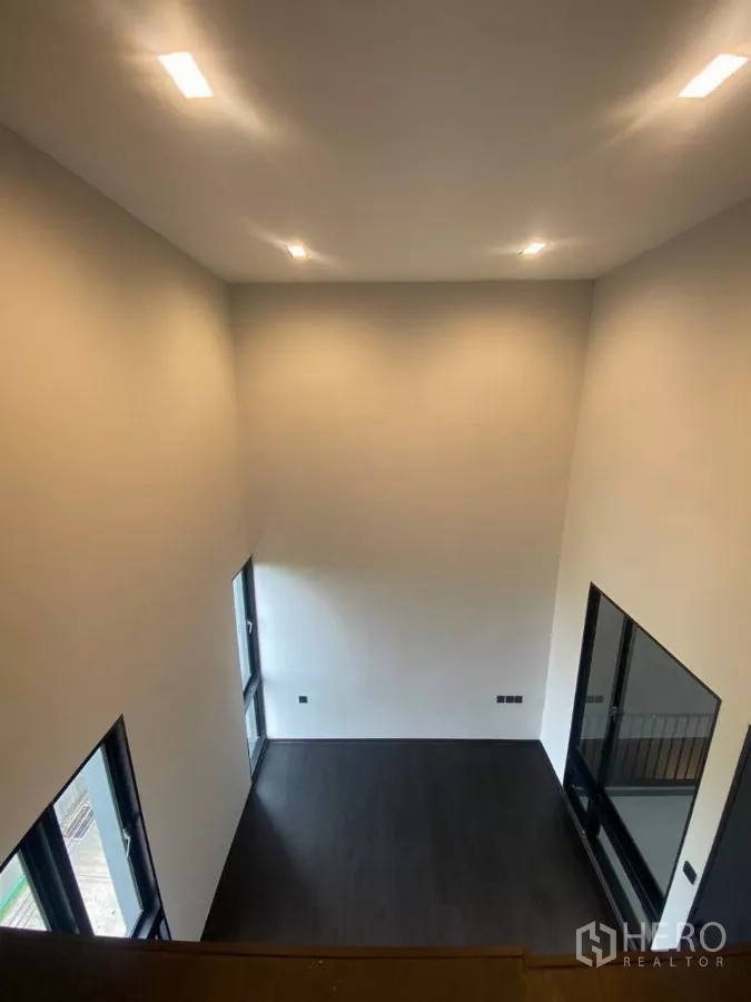 ทาวน์เฮาส์ ให้เช่าในHuai Khwang, Bangkok - มุมมองจากชั้นลอยสู่ห้องโปร่งเพดานสูง พื้นสีเข้มและหน้าต่างสูง.