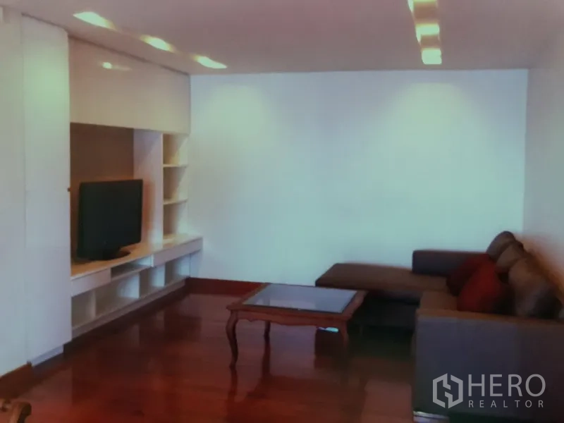 คอนโด ให้เช่าในWatthana, Bangkok - ห้องนั่งเล่นพร้อมผนังบิลท์อินวางทีวี โซฟาเข้ามุม ไฟฝังฝ้า และพื้นไม้ขัดเงา