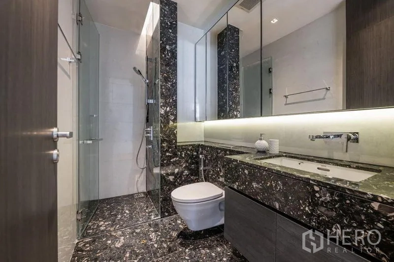 Condominium for rent in Khlong Toei, Bangkok - Second bathroom with glass-enclosed shower, backlit mirror and black marble counters.