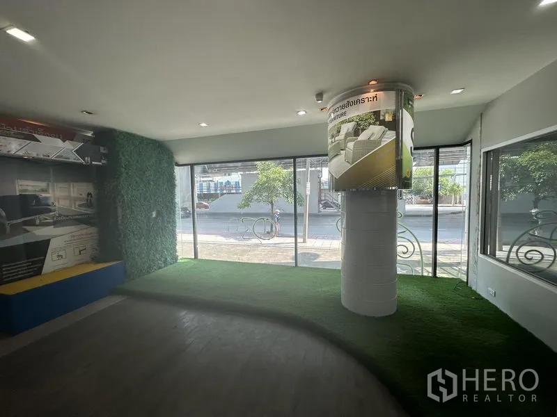 零售空间 出租在Suan Luang, Bangkok - 转角展示区，通高玻璃、柱体广告位与人造草坪台面。