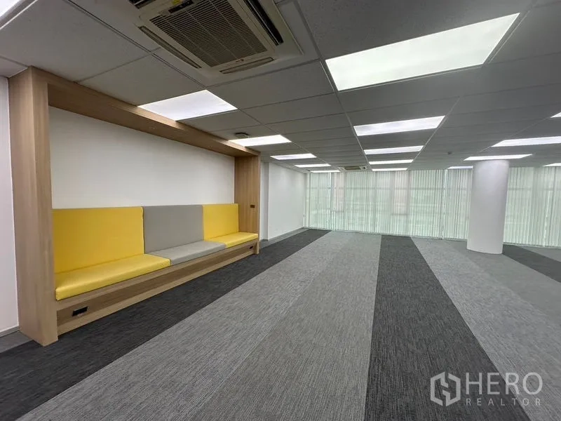 Office Space for rent - Breakout nook with cushioned seating beside open work area and windows.