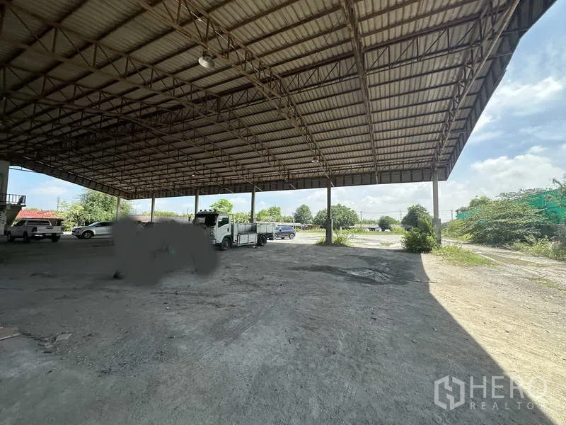 工厂 出租在Phra Nakhon Si Ayutthaya - 从开敞车棚望向宽阔场地，高顶棚下有卡车与停车位。