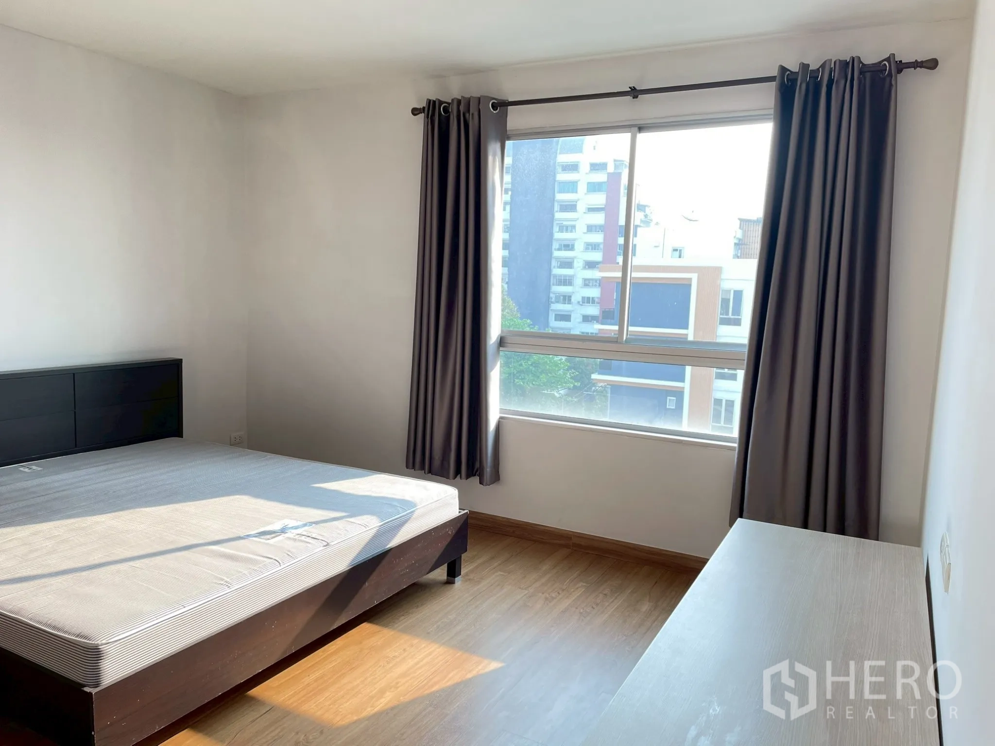 Apartment for rent in Khlong Toei, Bangkok - Bedroom with bed by a large window and blackout curtains.