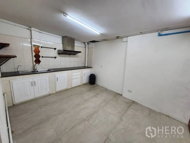 Home Office for rent in Khlong Toei, Bangkok - Functional kitchen with long black countertop, white base cabinets, sink, wall tiles, shelves, and a cooker hood.