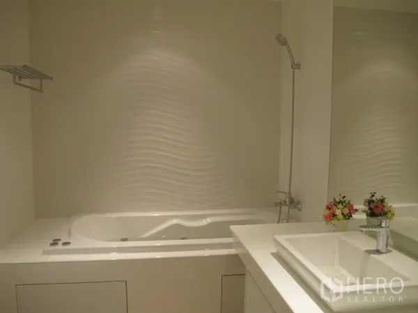 Condominium for rent in Watthana, Bangkok - Modern bathroom featuring a white soaking tub, wave-textured wall and vanity sink.
