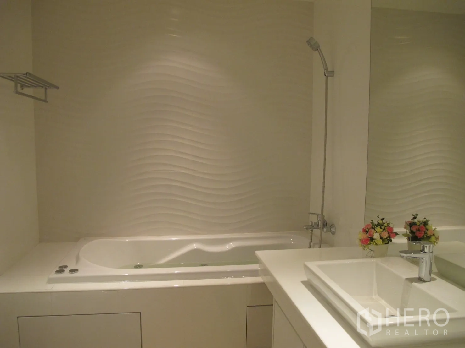 Condominium for rent in Watthana, Bangkok - Modern bathroom featuring a white soaking tub, wave-textured wall and vanity sink.