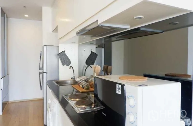 คอนโด ให้เช่าในBangkok - ครัวแบบแกลเลย์ เคาน์เตอร์สีดำ เตา ซิงก์ ไมโครเวฟ ตู้เย็น และเครื่องซักผ้า