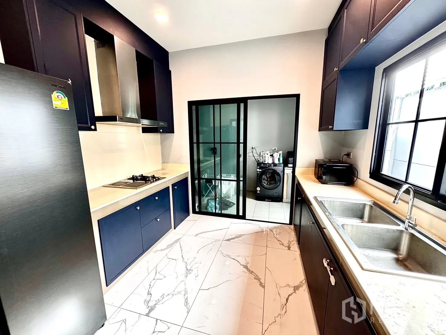 Detached House for rent in Bang Phli, Samut Prakan - Galley kitchen with navy cabinets, gas hob, stainless hood and sliding door to the laundry area.