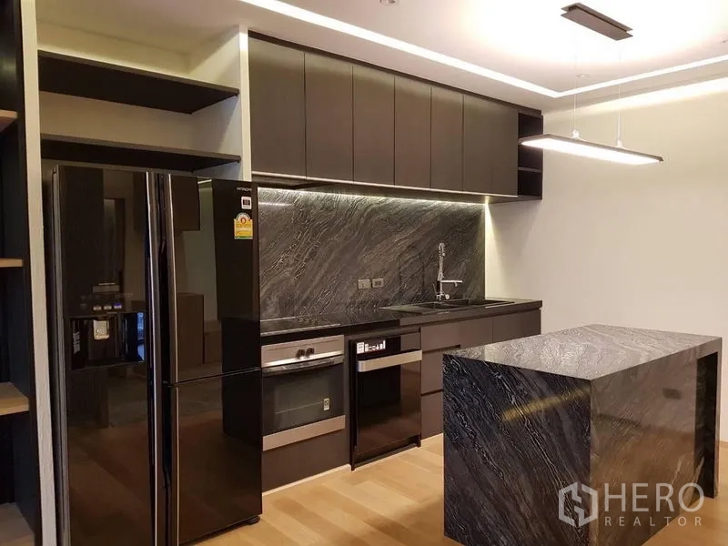 Condominium for rent in Bang Rak, Bangkok - Sleek kitchen featuring a black refrigerator, stone island and ample upper cabinetry.