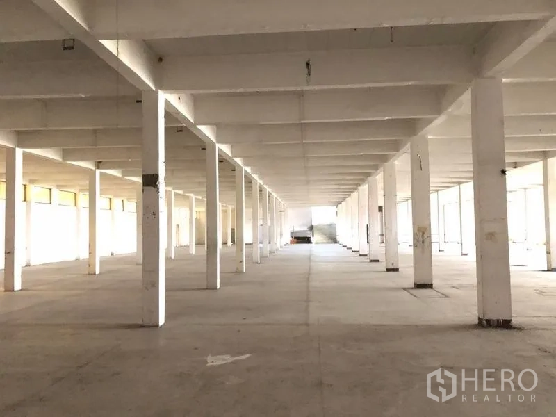 Factory for rent in Bang Phli, Samut Prakan - Deep view down a long columned factory hall with a loading ramp and daylight at the far end.
