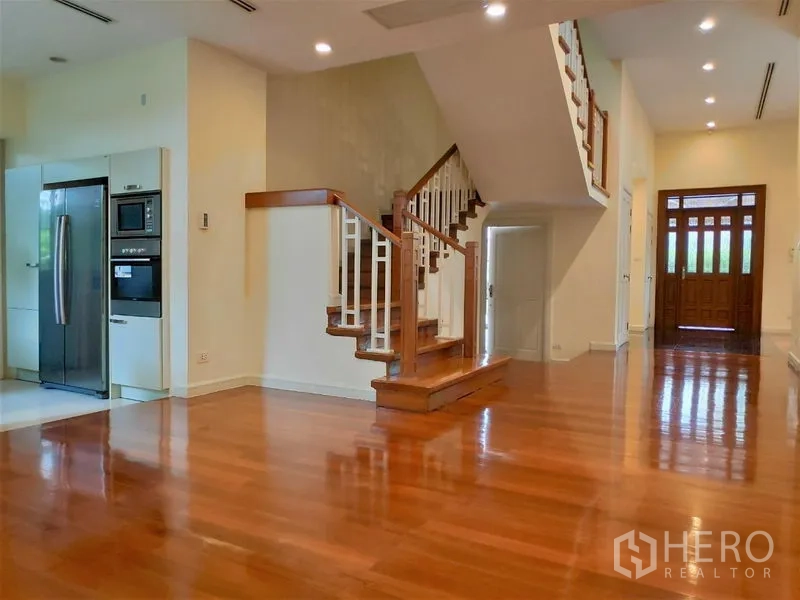 独立式住宅 出租在Watthana, Bangkok - 开放式起居区，亮面实木地板与木楼梯，嵌灯照明，旁为现代化厨房。