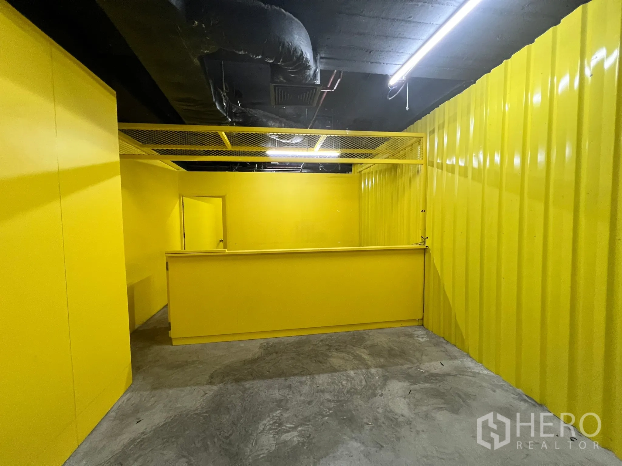 พื้นที่ขายปลีก ให้เช่า - โซนเคาน์เตอร์ต้อนรับ ผนังลอนสีเหลือง เพดานตะแกรง และไฟหลอดยาว