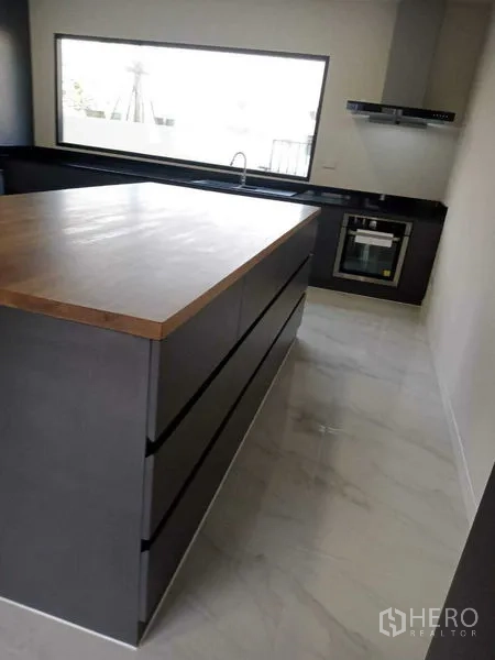 Townhouse for rent in Bang Phli, Samut Prakan - Modern kitchen with wood-top island, dark cabinets and built-in oven.