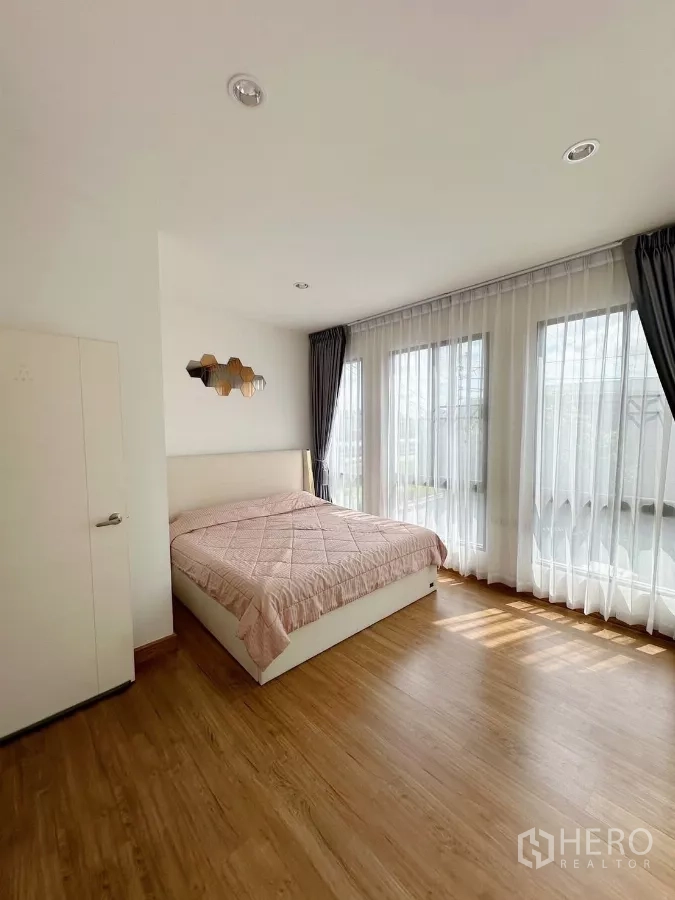 Townhouse for rent in Bang Phli, Samut Prakan - Sunlit master bedroom with wood floors and corner windows dressed with sheer curtains.