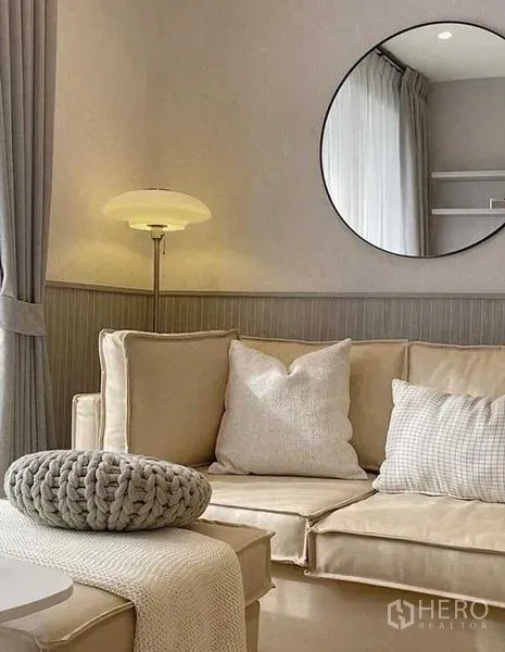Condominium for rent in Watthana, Bangkok - Close‑up of the sofa area with floor lamp, round mirror and textured cushions in neutral tones.