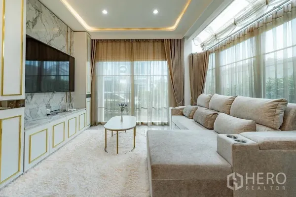 บ้าน ให้เช่าหรือขายในBang Khen, Bangkok - ห้องนั่งเล่นสวยหรู ผนังทีวีลายหินอ่อน โซฟาเบจ ไฟซ่อน และผ้าม่านสูงจรดเพดาน