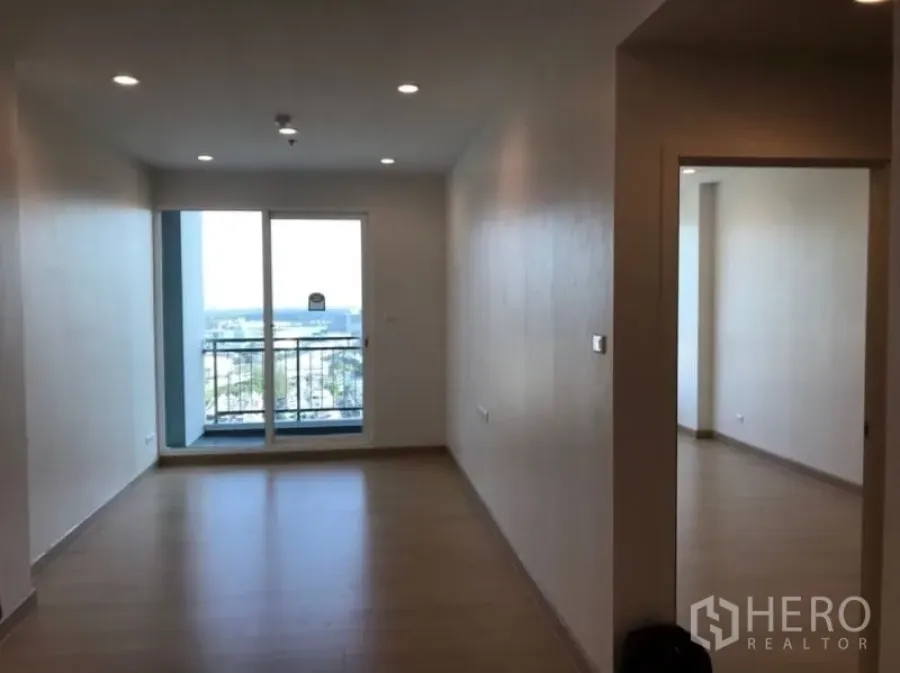 Condominium for sale in Yan Nawa, Bangkok - Bright unfurnished living room with wood floors, recessed lights, and sliding glass doors opening to a balcony with city view.