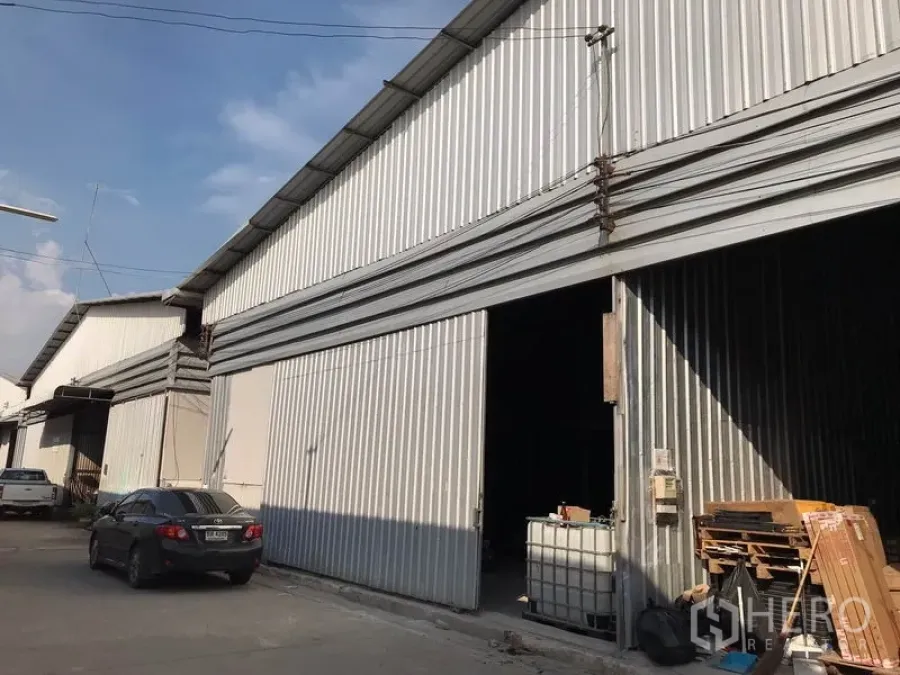 คลังสินค้า ให้เช่าในMueang Samut Prakan, Samut Prakan - ด้านหน้าโกดังผนังเมทัลชีท ประตูบานเลื่อนกว้าง มีที่จอดรถและสายไฟเหนือทางเข้าในซอยอุตสาหกรรมย่านเมืองสมุทรปราการ