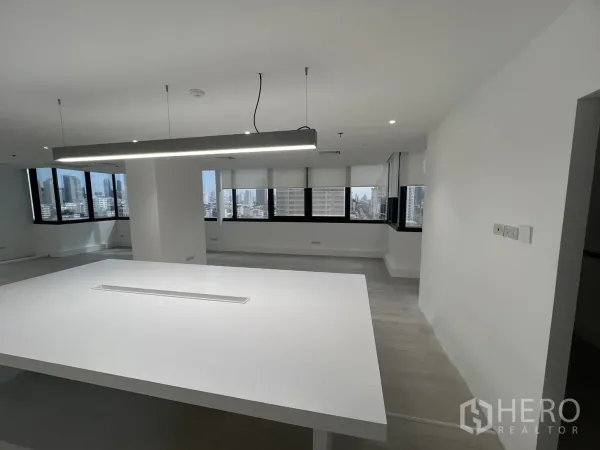Office Space for rent in Khlong Toei, Bangkok - Central worktable under a linear pendant facing panoramic windows with Bangkok skyline views.