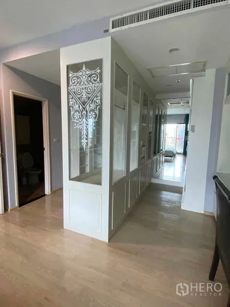 Condominium for rent in Khlong Toei, Bangkok - Hallway with glass-front wardrobes and a decorative panel leading toward the living area.