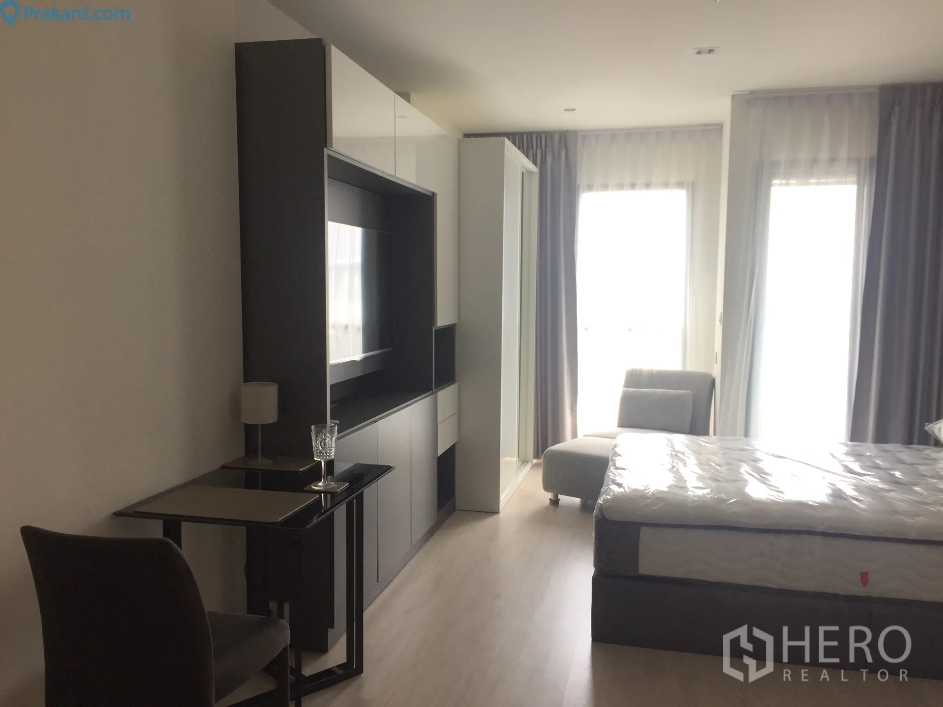 Condominium for rent in Ratchathewi, Bangkok - Bright studio layout with bed, media cabinet, small dining desk and large curtained windows.