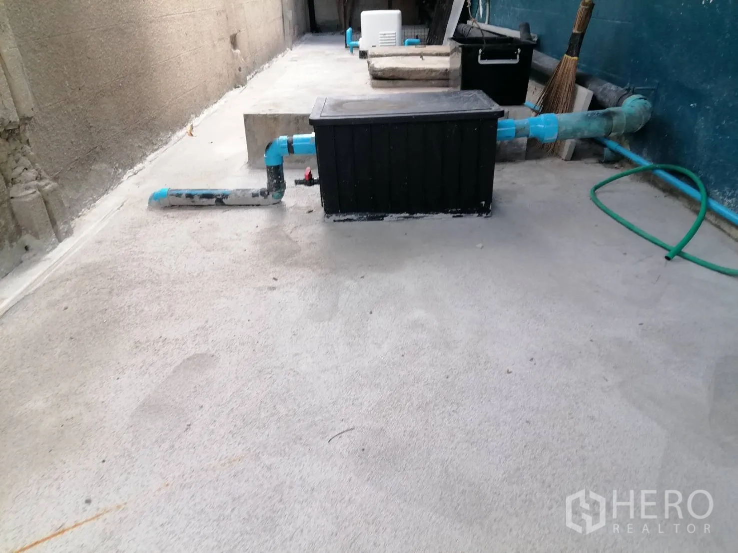 Detached House for rent in Watthana, Bangkok - Outdoor utility zone with a black grease trap box and blue plumbing pipes on a concrete surface.