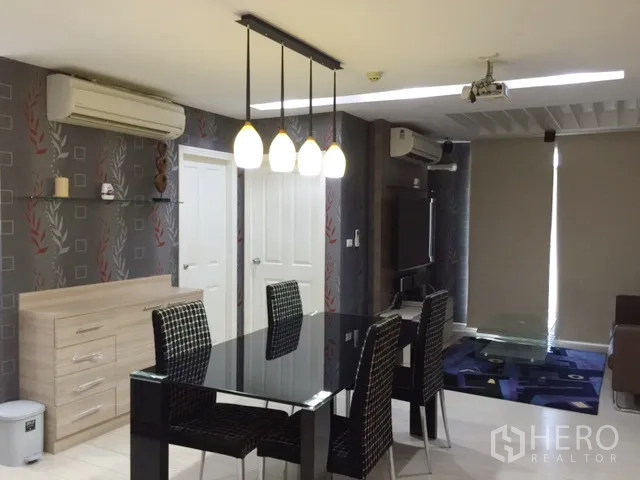 คอนโด ให้เช่าหรือขายในKhlong Toei, Bangkok - ห้องนั่งเล่นและรับประทานอาหารพร้อมโคมไฟห้อย โต๊ะกระจกสีดำ ทีวีติดผนัง และเครื่องปรับอากาศ