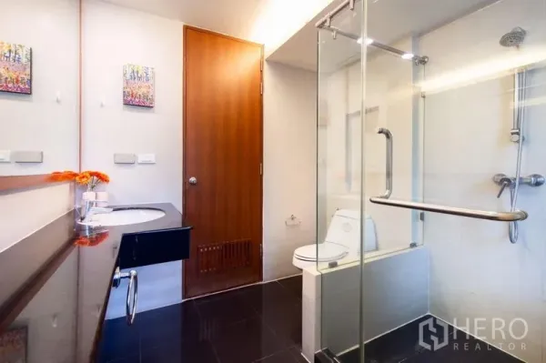 Condominium for rent in Bang Rak, Bangkok - Modern bathroom featuring a glass-enclosed shower, toilet and black countertop vanity.