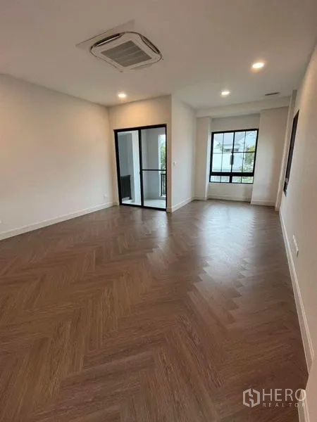 Detached House for rent in Saphan Sung, Bangkok - Spacious bedroom with herringbone flooring, large windows and a sliding glass door.