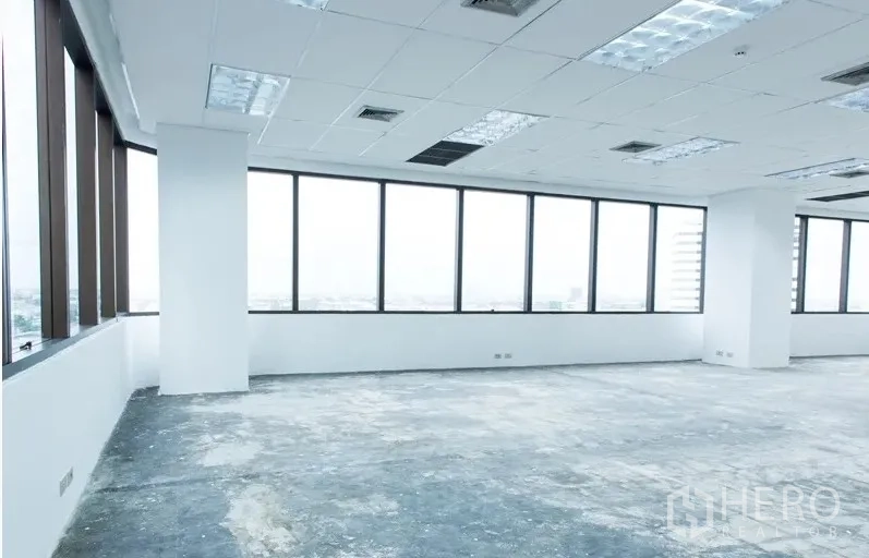 Office Space for rent in Bang Na, Bangkok - Bright corner open-plan office with wraparound windows, suspended ceiling lights, and an unfinished floor with city views.