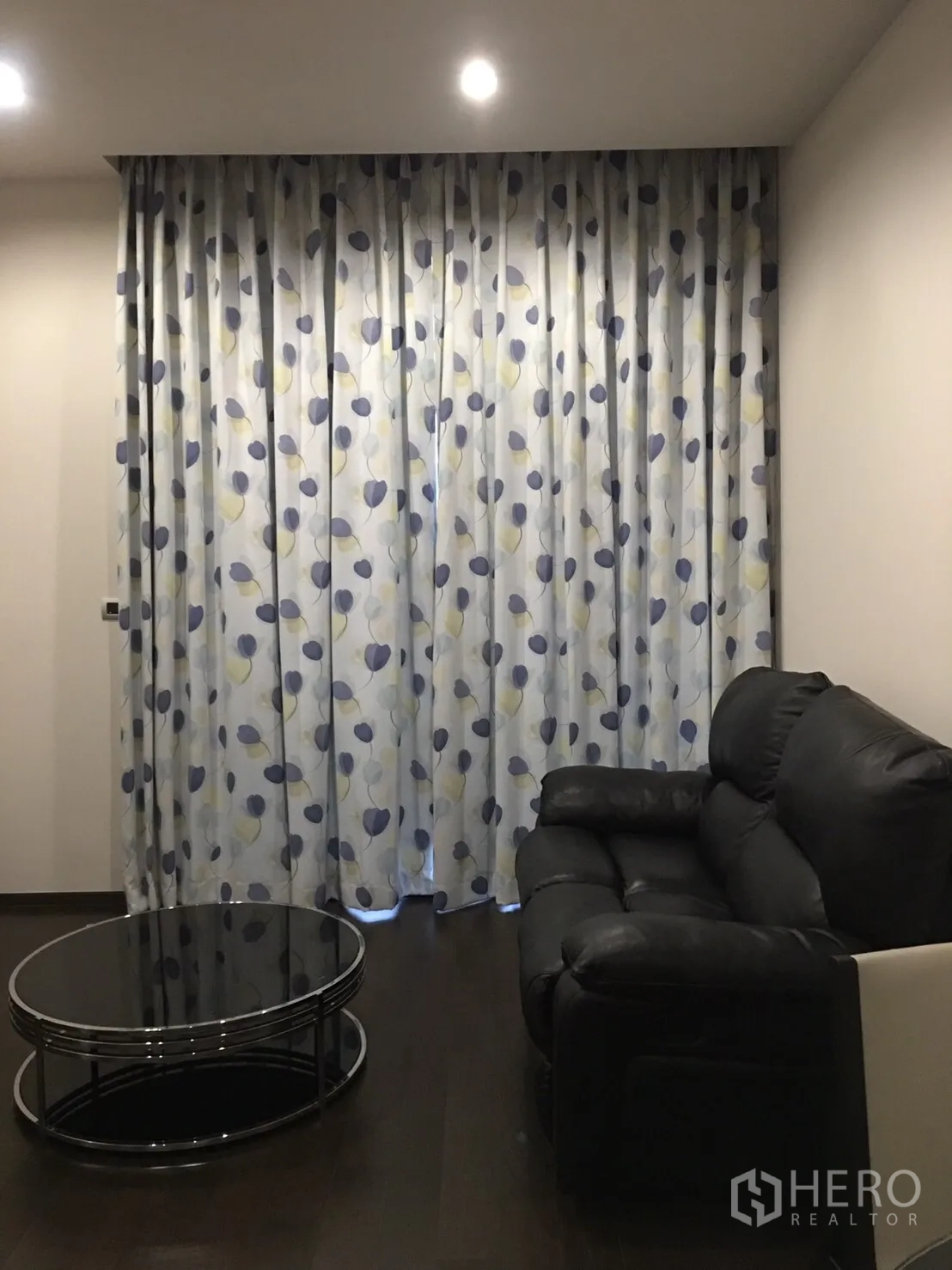 Condominium for rent in Watthana, Bangkok - Cozy lounge with black recliner sofa, circular glass coffee table, and patterned curtains under recessed lighting.