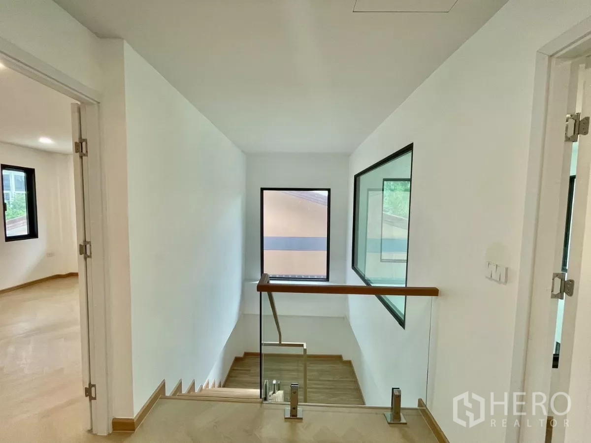 独立式住宅 出售在Prawet, Bangkok - 二层平台，玻璃栏杆、大窗与浅色木地板。