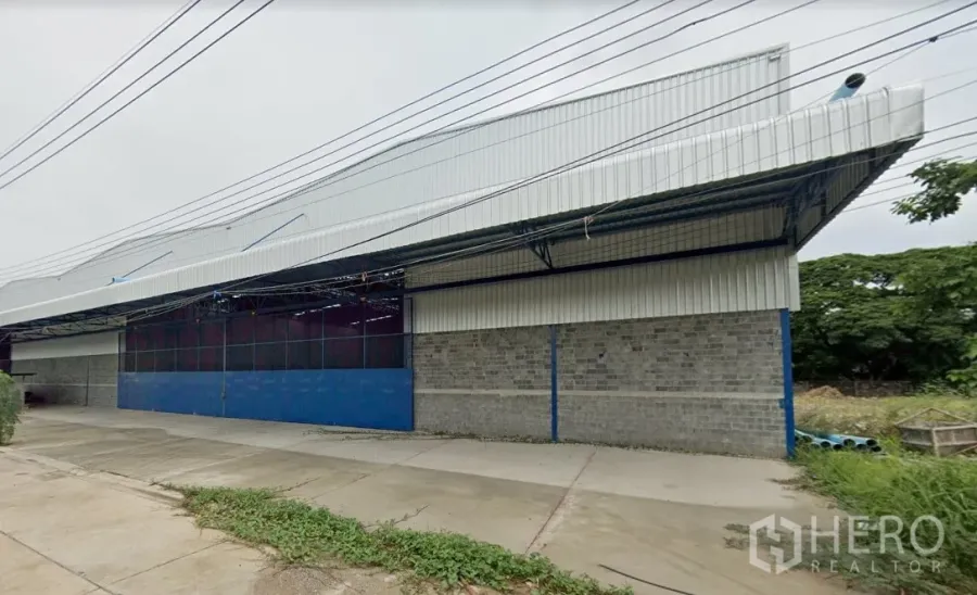 Warehouse for rent in Min Buri, Bangkok - Steel-clad warehouse exterior in Min Buri, Bangkok with high gabled roof, blue sliding gate, and wide concrete loading apron.